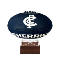 A Carlton BLues AFL football urn with a white logo and 'SHERRIN' text, mounted on a clear acrylic stand with a dark wood base against a white background.