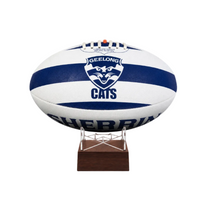 A white and navy blue Geelong Cats AFL ball displayed on a small wooden stand against a plain white background.