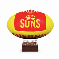 A yellow and red GC Suns football displayed on a clear stand with a dark brown wooden base against a white background.
