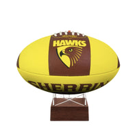 A yellow and brown Sherrin Hawks football displayed on a small wooden stand against a white background.