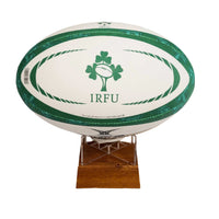 A white rugby ball with green trim and a green shamrock logo with the text 'IRFU' on the front, displayed on a small wooden stand against a plain white background.