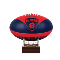 A red and navy blue Melbourne Football Club AFL ball urn displayed on a clear acrylic stand with a dark wood base against a white background.