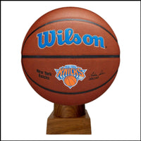 A handcrafted cremation urn made from an authentic New York Knicks basketball displayed on a wooden base with a blue and orange bow on top.