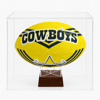 A yellow football urn with 'COWBOYS' lettering displayed inside a clear acrylic case on a wooden stand.