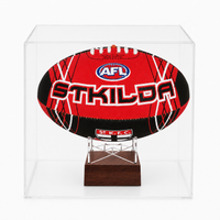 A red and black AFL football with 'STKILDA' printed across the front, displayed inside a clear acrylic case on a small wooden stand.
