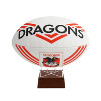 A white St. George Dragons rugby ball displayed on a clear acrylic stand with a dark brown wooden base against a plain white background.