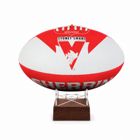 A red and white Sydney Swans AFL ball urn displayed on a clear acrylic stand with a dark brown wooden base, set against a plain white background.