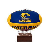 A West Coast Eagles AFL ball urn displayed on a clear acrylic stand with a dark wood base, set against a plain white background.