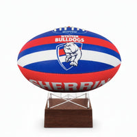 A Western Bulldogs AFL ball urn displayed on a clear acrylic stand with a dark brown wooden base, set against a plain white background.