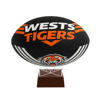 A black Wests Tigers rugby ball displayed on a clear acrylic stand with a dark brown wooden base, set against a plain white background.