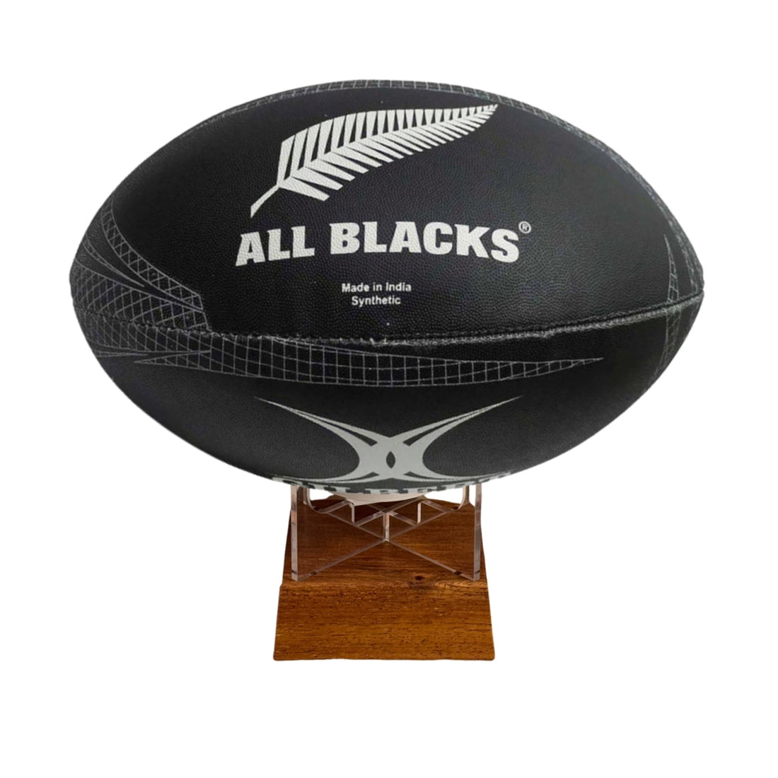A black All Blacks rugby ball with silver fern and white branding, displayed on a small wooden stand against a plain white background.