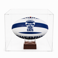 A Geelong Cats afl ball urdisplayed inside a clear acrylic cube case on a small wooden stand, photographed against a clean white background.