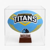 A light blue and yellow Gold Coast Titans rugby ball displayed inside a clear acrylic display case on a dark wood stand.