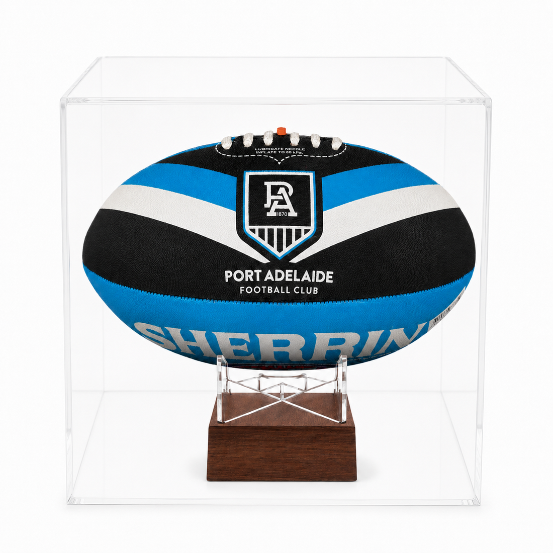 A Port Adelaide Football Club rugby ball displayed inside a clear acrylic cube case on a wooden stand.