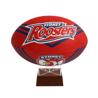 A red Sydney Roosters rugby ball urn displayed on a clear acrylic stand with a dark wood base against a plain white background.