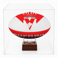 A cremation urn designed to look like a Sydney Swans AFL football with red and white stripes, featuring the Sydney Swans logo and the year 1914 on the upper part inside a clear acrylic display case on a dark wood stand, photographed against a clean white background.