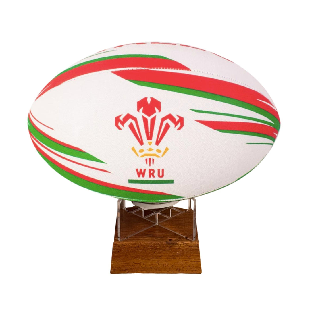 A white rugby ball with red and green stripes and the Welsh Rugby Union (WRU) logo, displayed on a small wooden stand against a plain white background.