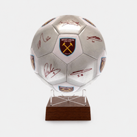 A silver West Ham United soccer ball with multiple autographs and team crests, mounted on a clear acrylic stand with a dark brown wooden base against a light gray background.